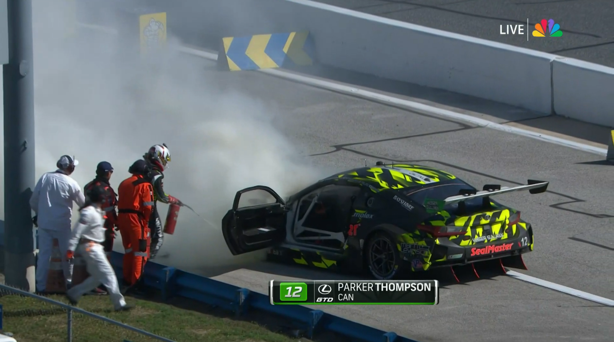 A driver futilely tries to extinguish a fire billowing from the hood of a Lexus race car.