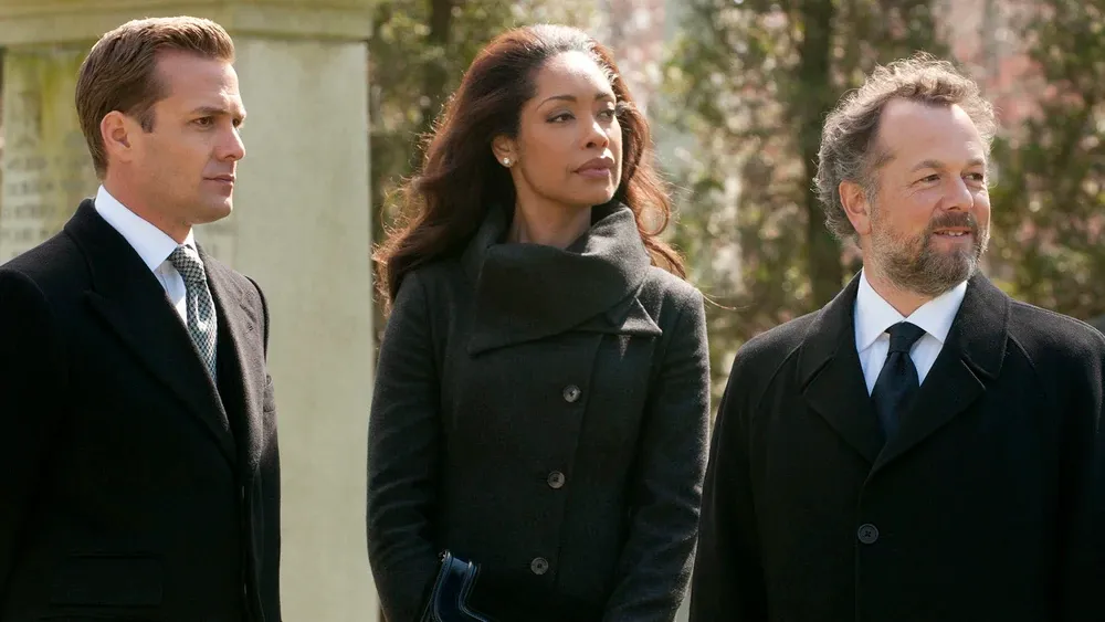 Gabriel Macht, Gina Torres, and David Costabile standing in funereal wool jackets on a fall day.